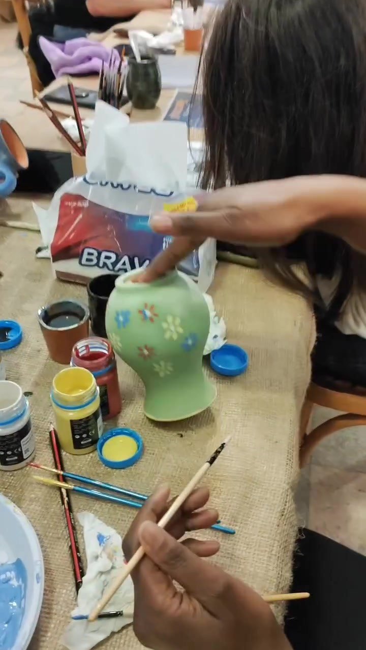Painting small flowers onto a green ceramic vase with underglaze paints at a pottery painting workshop in Amman