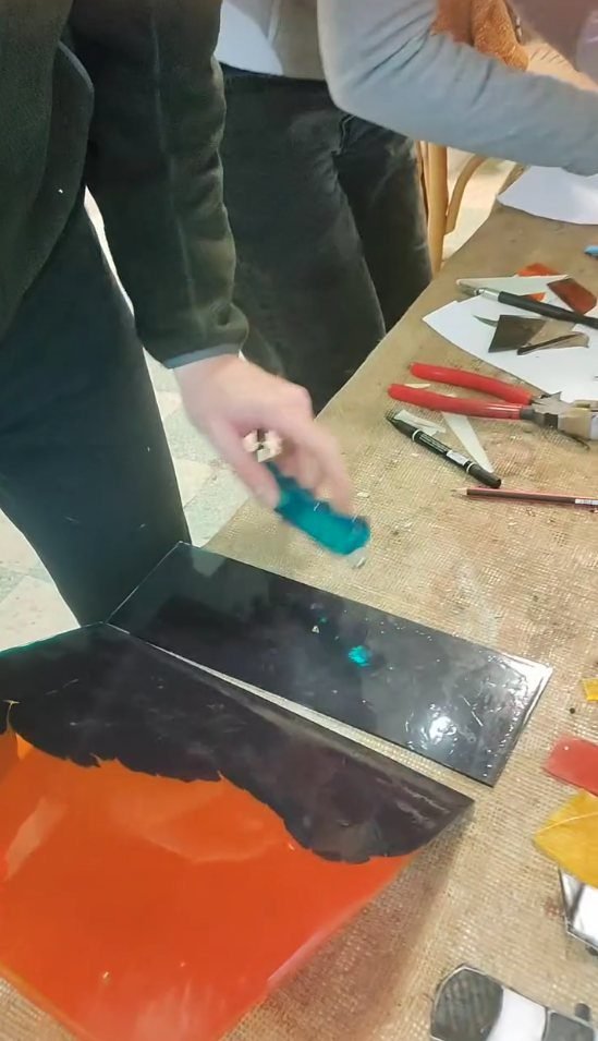 Hands cutting a sheet of green glass with a glass cutter in an Amman stained glass class