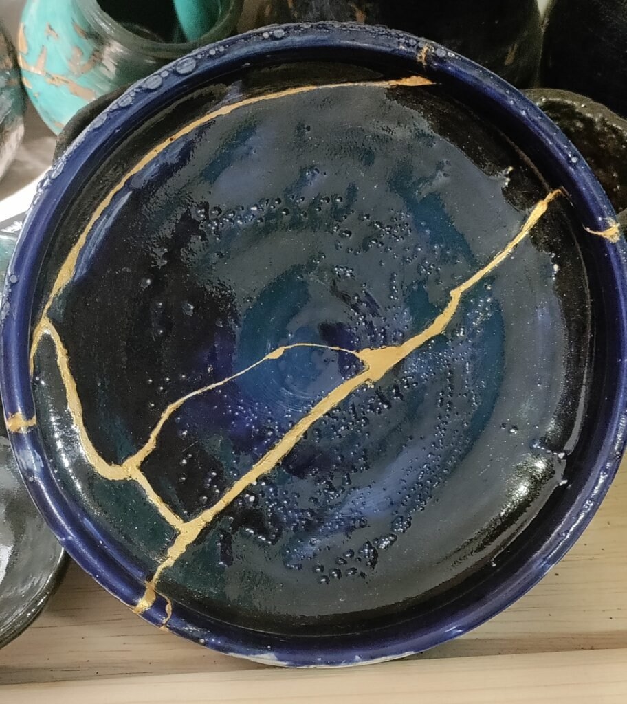 A blue glazed bowl repaired with kintsugi, gold seams running along the break lines