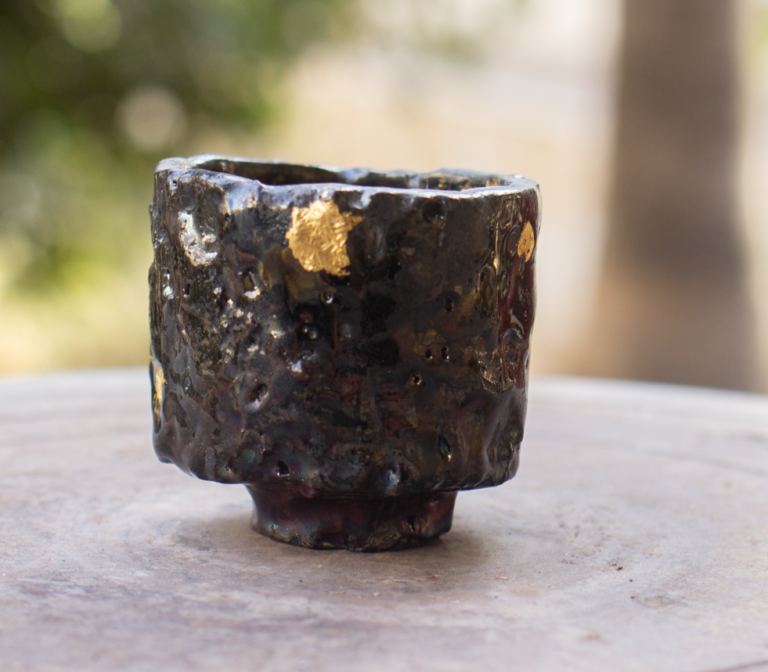 A dark raku tea bowl repaired with gold along the rim