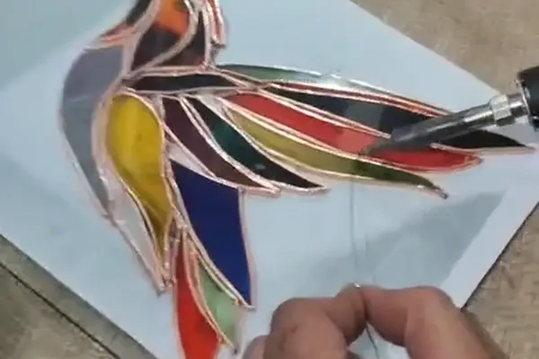 A stained glass hummingbird being soldered at Gilgamesh